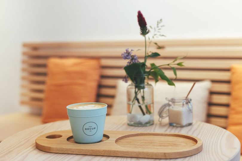 Eine Sitzecke im Café auf dem Tisch eine Vase mit Blumen, Zucker und ein Kaffee im Recup Becher