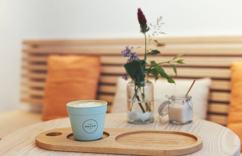 Eine Sitzecke im Café auf dem Tisch eine Vase mit Blumen, Zucker und ein Kaffee im Recup Becher