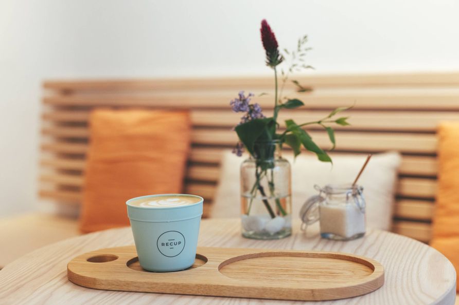 Eine Sitzecke im Café auf dem Tisch eine Vase mit Blumen, Zucker und ein Kaffee im Recup Becher