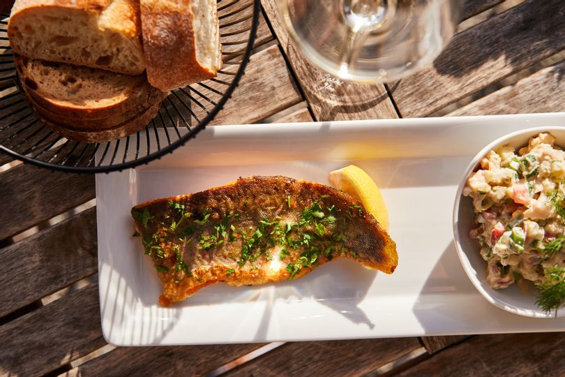 Ein Teller schön hergerichtet mit Fisch und Salat. Daneben ein Brotkorb.