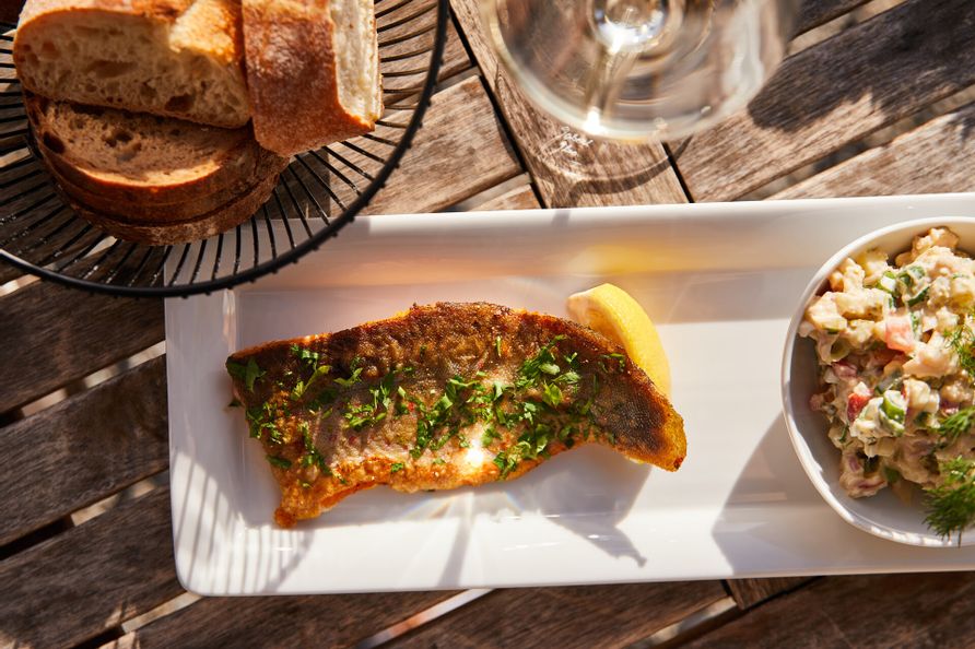 Ein Teller schön hergerichtet mit Fisch und Salat. Daneben ein Brotkorb.