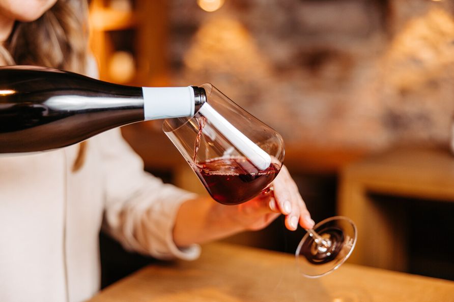 Eine Frau hält ein Weinglas in der Hand und schenkt Rotwein ein