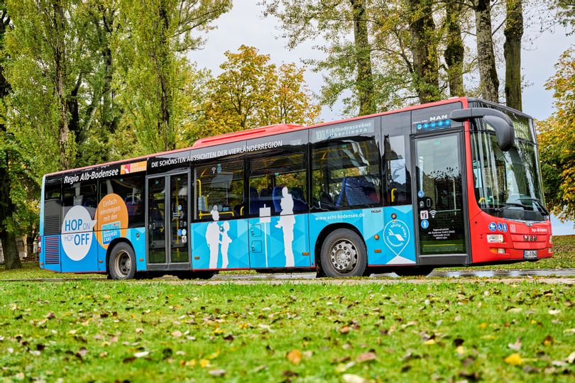 Ein Bus inmitten von grün. Im Vordergrund eine Wiese im Hintergrund Bäume.