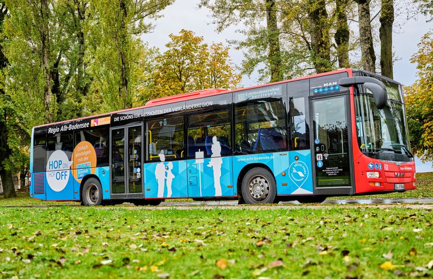 Ein Bus inmitten von grün. Im Vordergrund eine Wiese im Hintergrund Bäume.