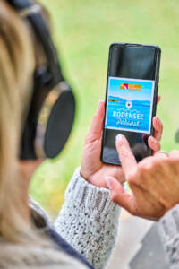 Eine Frau, die ihr Handy in der Hand hält und den Bodensee Podcast anhört.