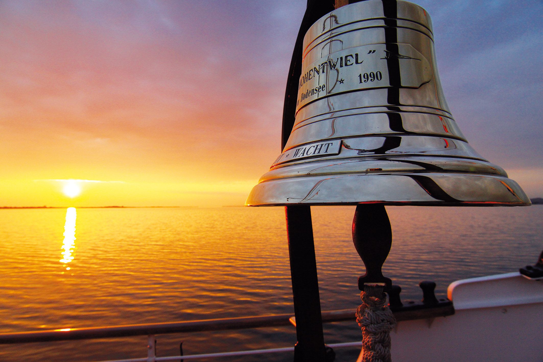 Glocke vom historischen Dampfschiff Hohentwiel im Hintergrund der Sonnenuntergang auf dem See