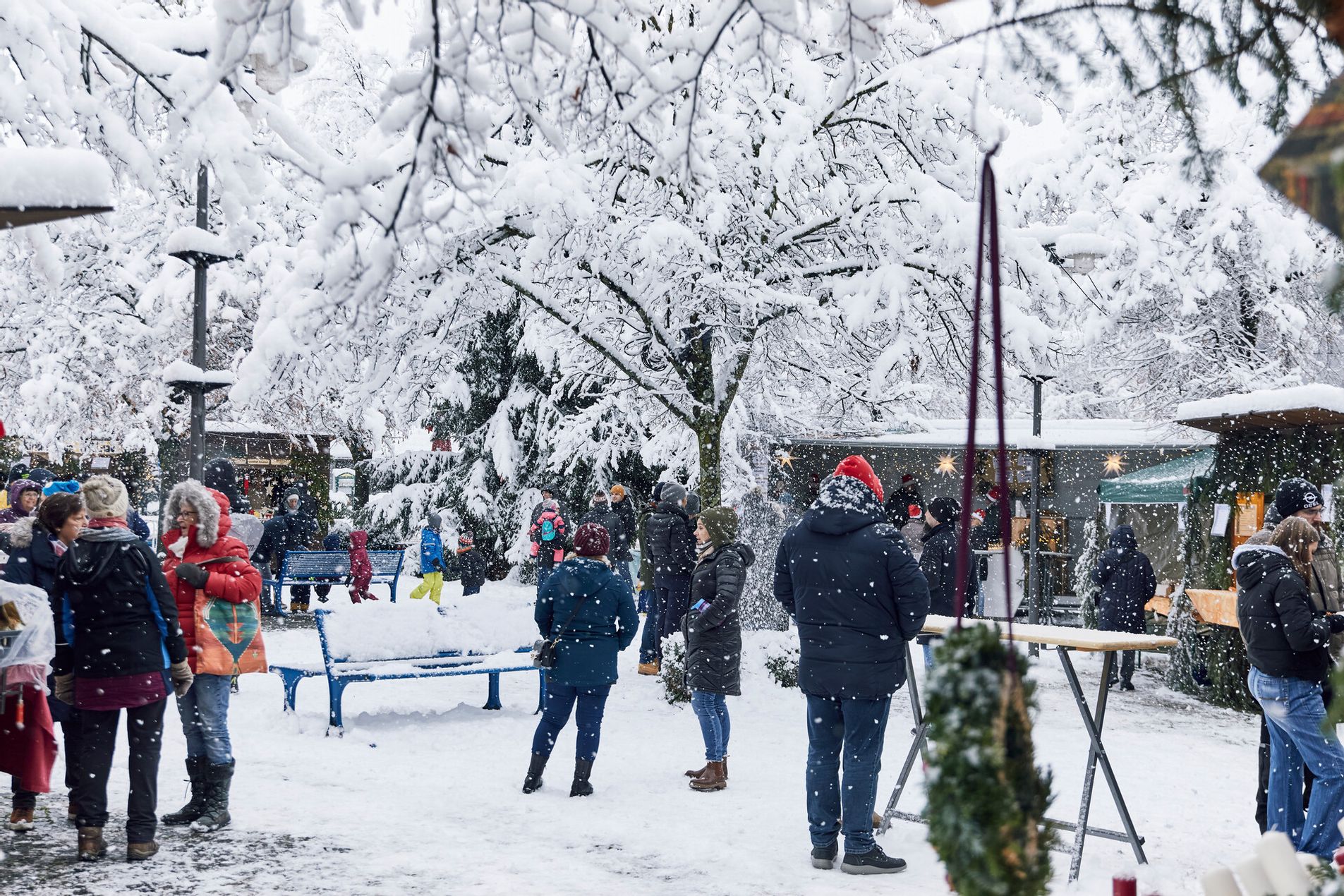 Mehrere Personen die den Adventsmarkt in Wasserburg besuchen. Es schneit und der Boden sowie Bäume sind komplett verschneit.
