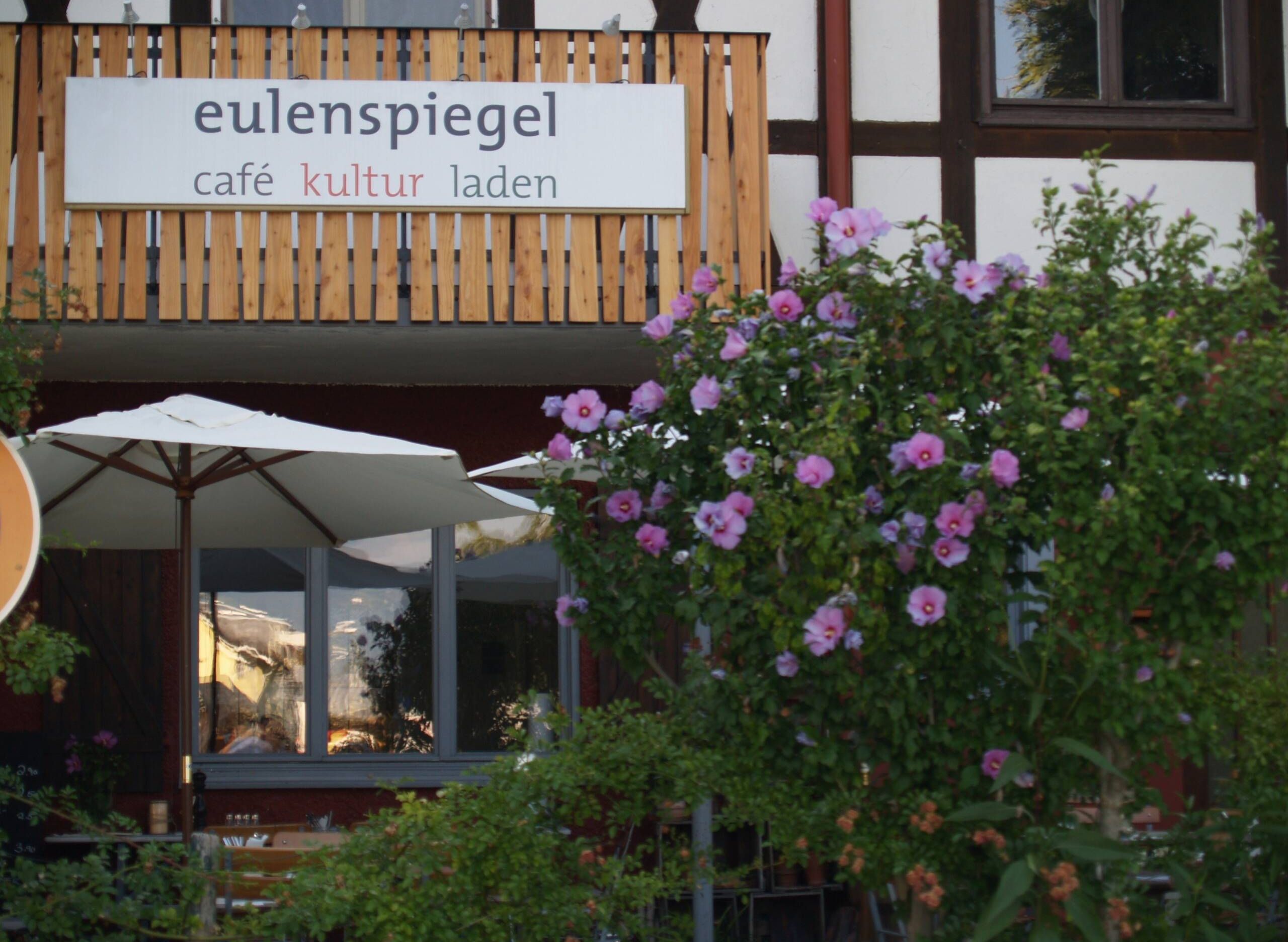 Außenansicht Restaurant und Café Eulenspiegel. Blick auf Terrasse mit blühendem Hibiskus im Vordergrund.