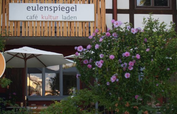 Außenansicht Restaurant und Café Eulenspiegel. Blick auf Terrasse mit blühendem Hibiskus im Vordergrund.
