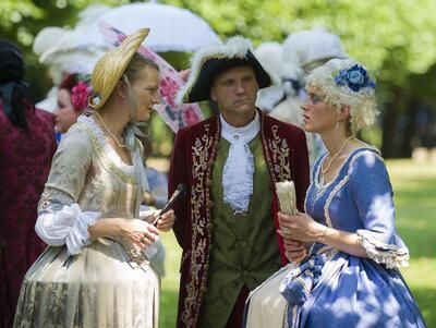 Personen in detailreichen Rokoko-Kostümen flanieren vor der beleuchteten Orangerie während der Ansbacher Rokoko-Festspiele.