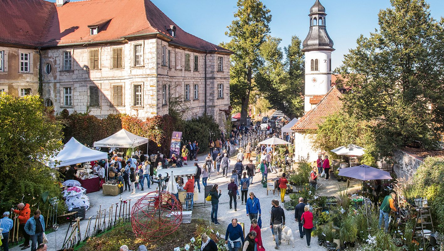 Besucher genießen den Gartenmarkt „Faszination Garten“ vor der malerischen Kulisse von Schloss Weingartsgreuth in Frankenrühlingsstimmung beim Gartenmarkt Franken 2026 auf Schloss Weingartsgreuth: Besucher schlendern durch blühende Stände, entdecken Pflanzenraritäten und genießen die besondere Atmosphäre im Steigerwald bei Wachenroth in Bayern