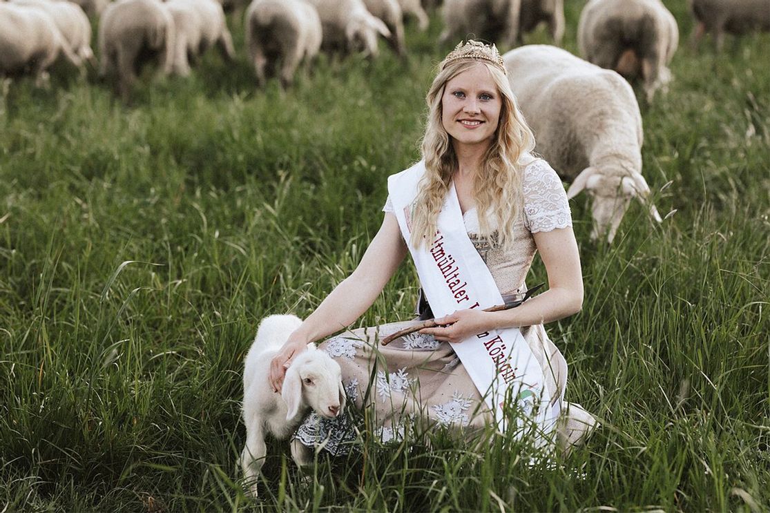Die amtierende Lammkönigin Annemarie Mack kniet in einer Wiese, umgeben von Lämmern und Schafen beim Altmühltaler Lamm-Abtrieb.