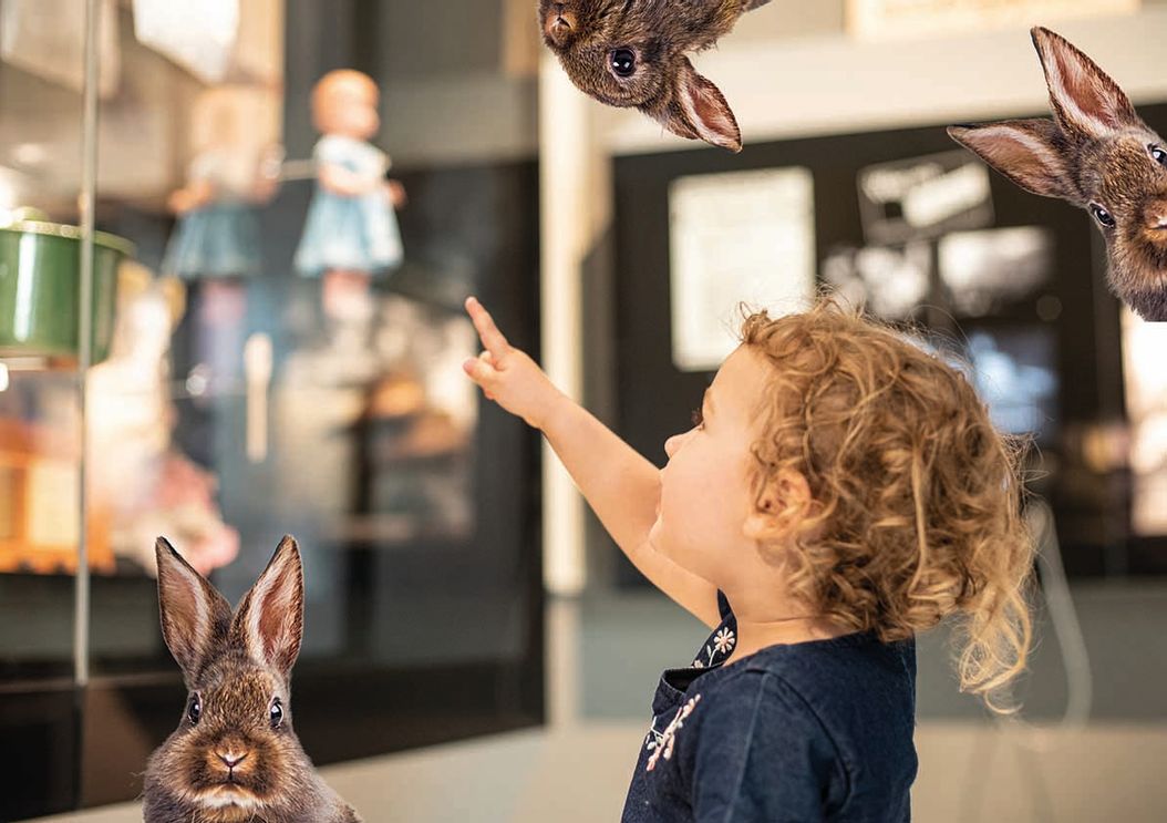 Das Bild zeigt ein Kind, das begeistert mit dem Osterhasen im Ludwig-Erhard Zentrum Fürth posiert, während im Hintergrund die fröhliche Umgebung der Ostereiersuche zu sehen ist.