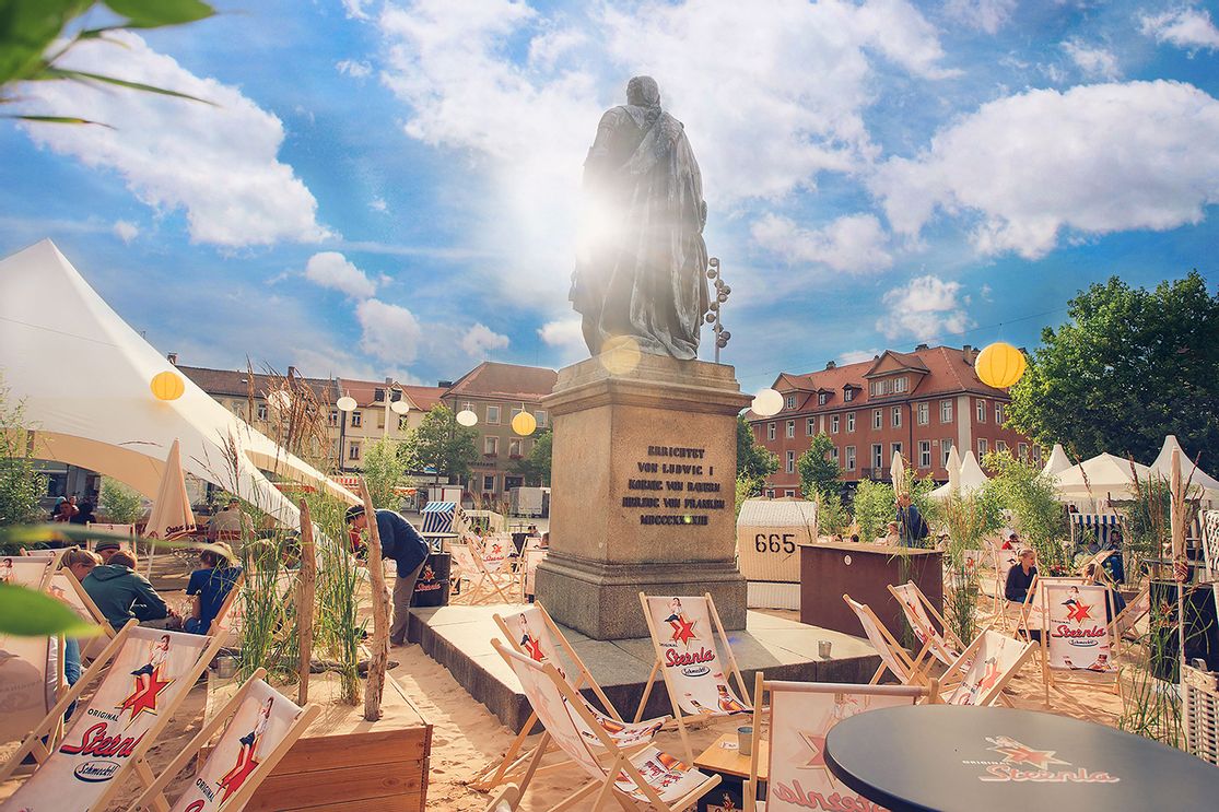 Besucher entspannen auf Liegestühlen und in Strandkörben am sonnigen Sternla SchlossStrand Erlangen.