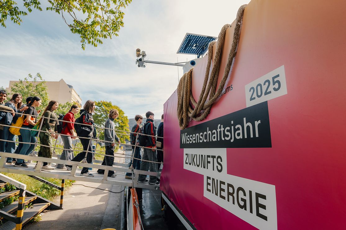 ine Gruppe Jugendlicher betritt über eine Gangway das Ausstellungsschiff MS Wissenschaft in Nürnberg, auf dessen pinker Außenwand „Wissenschaftsjahr 2025 Zukunftsenergie“ steht.