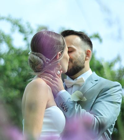 Ein Brautpaar, das sich küsst, als Inspiration von der Hochzeitsmesse Forchheim. Der Bräutigam im hellen Anzug umarmt die Braut mit Perlen in ihrer Hochsteckfrisur.