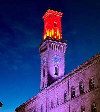Das Rathaus Fürth bei Nacht, eindrucksvoll beleuchtet für die Fürther Glanzlichter. Der Turm leuchtet feurig rot, während das Gebäude lila angestrahlt wird.