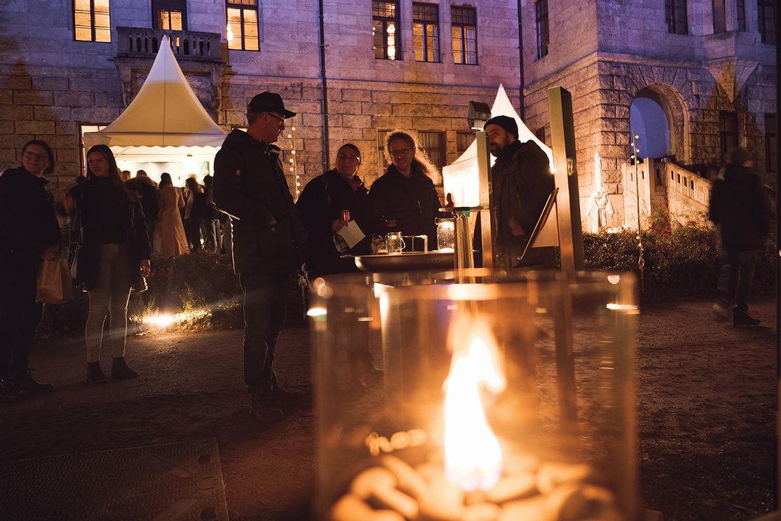 Besucher der Winterträume 2025 wärmen sich an einer Feuerstelle im Schlosshof des Faber-Castell'schen Schlosses und genießen die abendliche Atmosphäre.