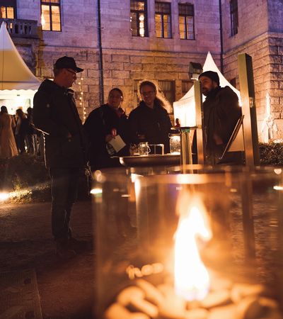Besucher der Winterträume 2025 wärmen sich an einer Feuerstelle im Schlosshof des Faber-Castell'schen Schlosses und genießen die abendliche Atmosphäre.