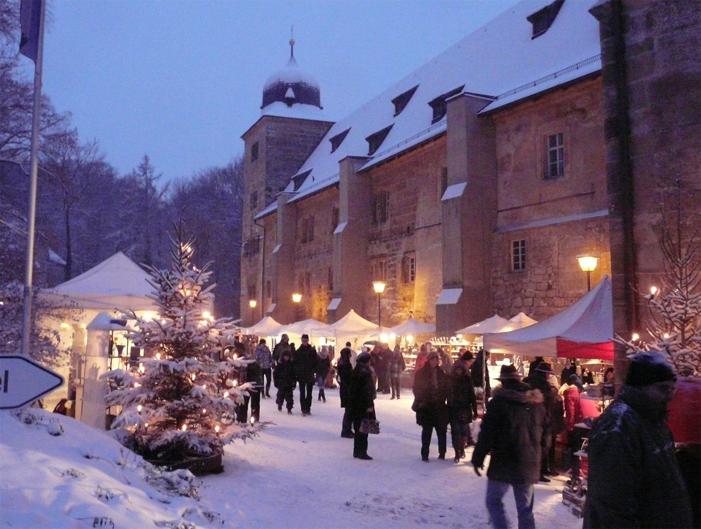 Weihnachtstöpfermarkt im verschneiten Schloss Thurnau mit beleuchteten Keramikständen, Besuchern und historischer Sandsteinarchitektur in Oberfranken.
