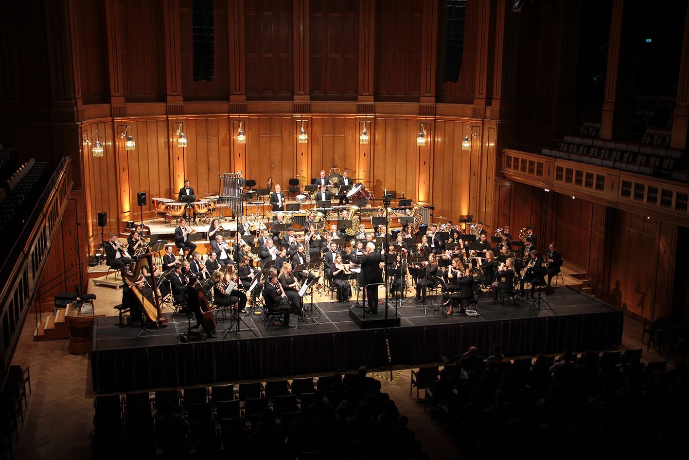 Großes symphonisches Blasorchester und Chor bei einer Konzertaufführung auf einer beleuchteten Bühne.