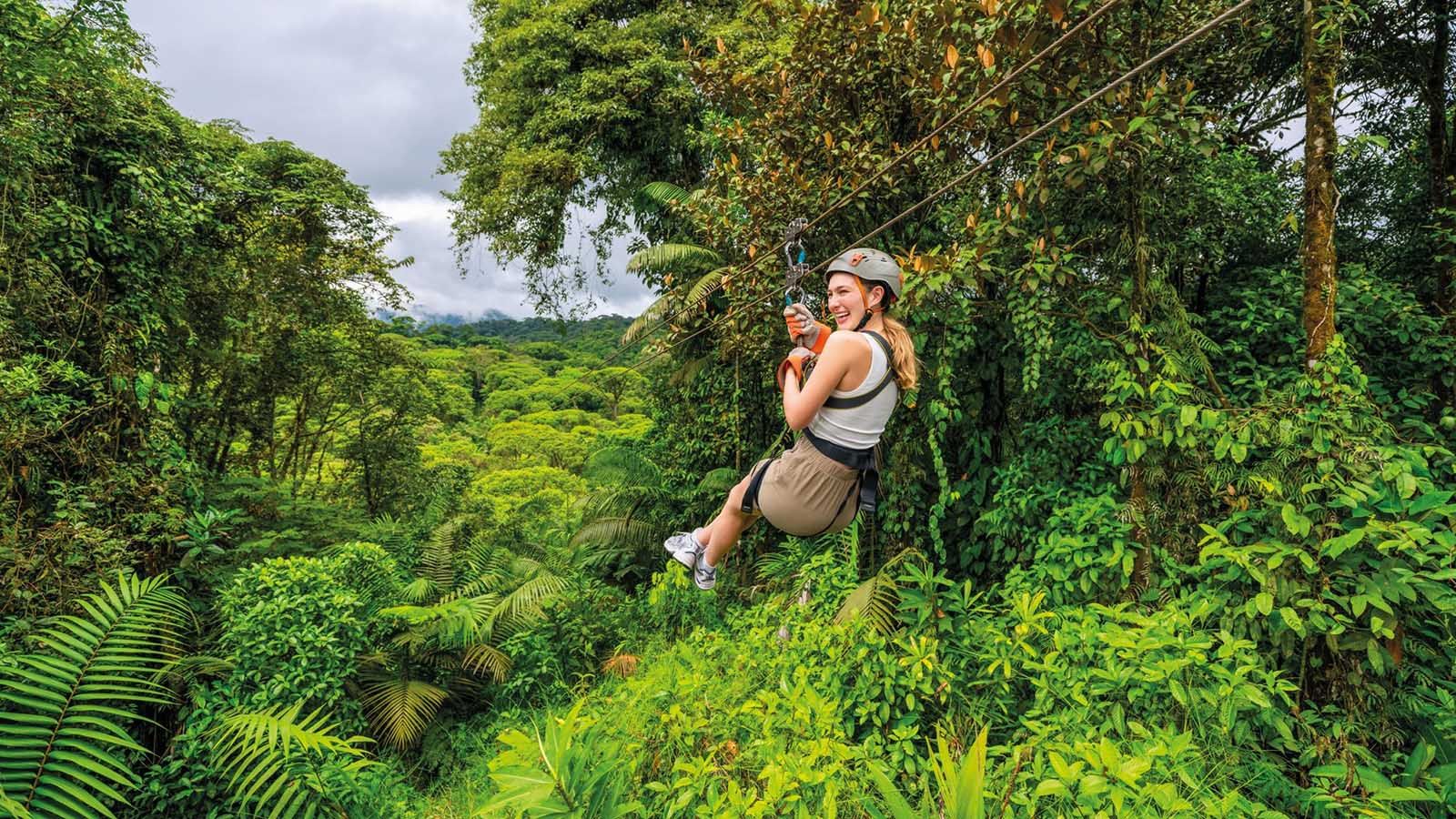 Eine Frau mit Helm und Klettergurt fährt an einer Zipline über dichten tropischen Regenwald.