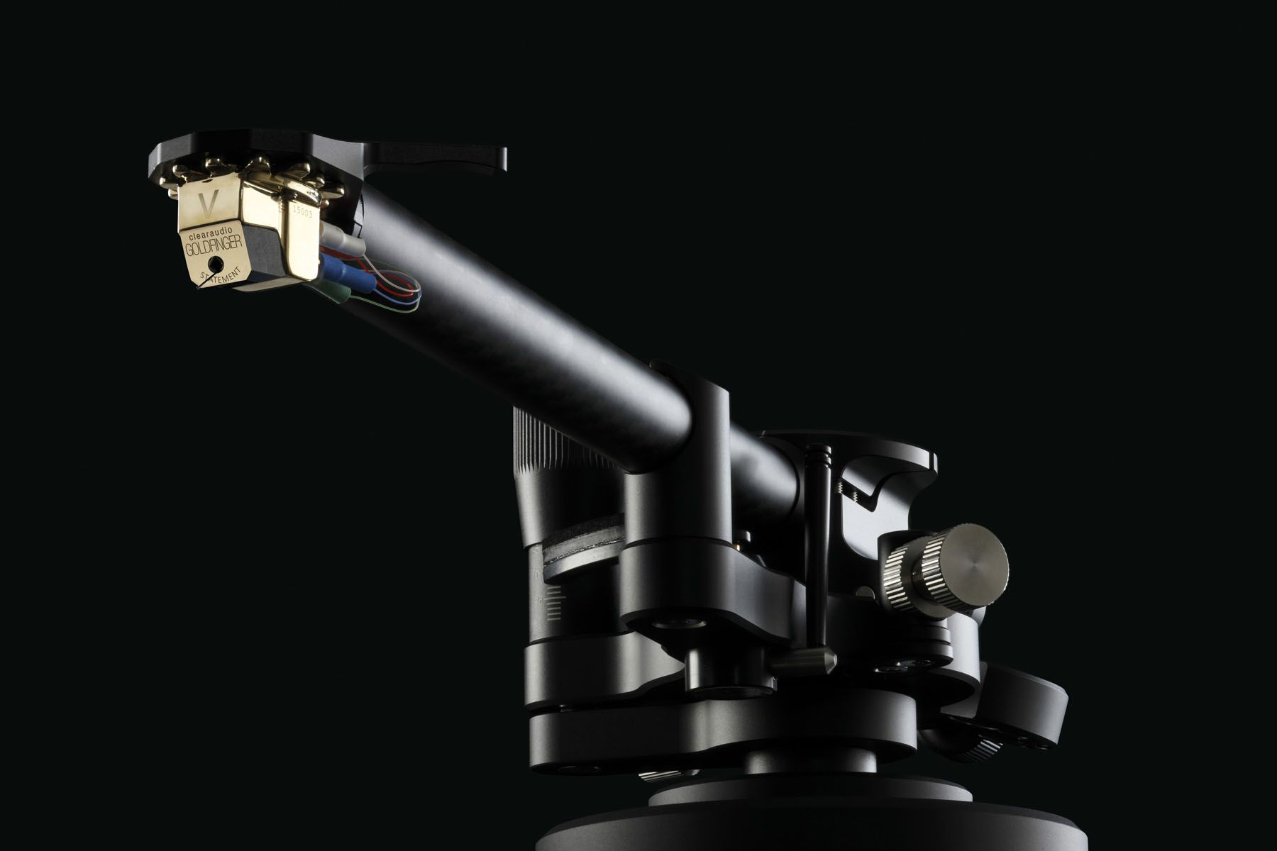 Side close-up of the gold clearaudio Goldfinger Statement V2.1 cartridge, mounted on the headshell of the black TA-Unity tonearm against a black background.