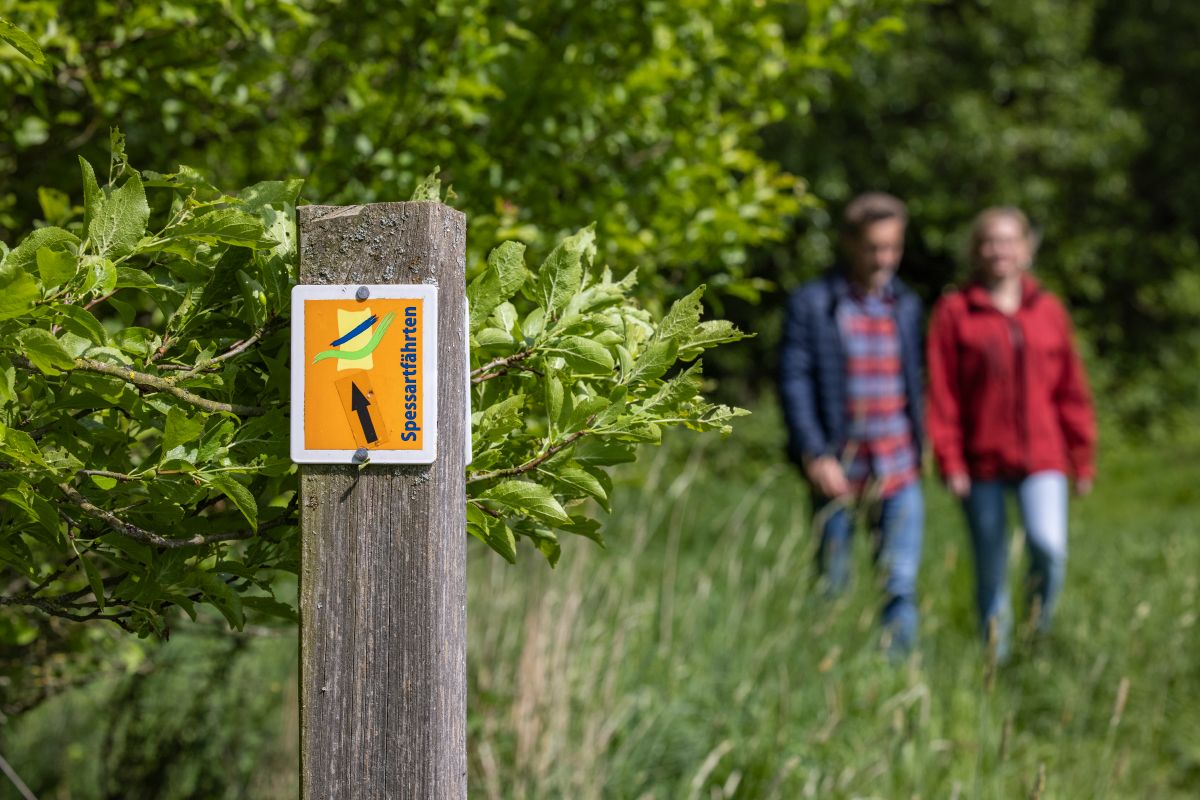 Ein Paar wandert über einen Wiesenpfad mit orangefarbener Wandermarkierung