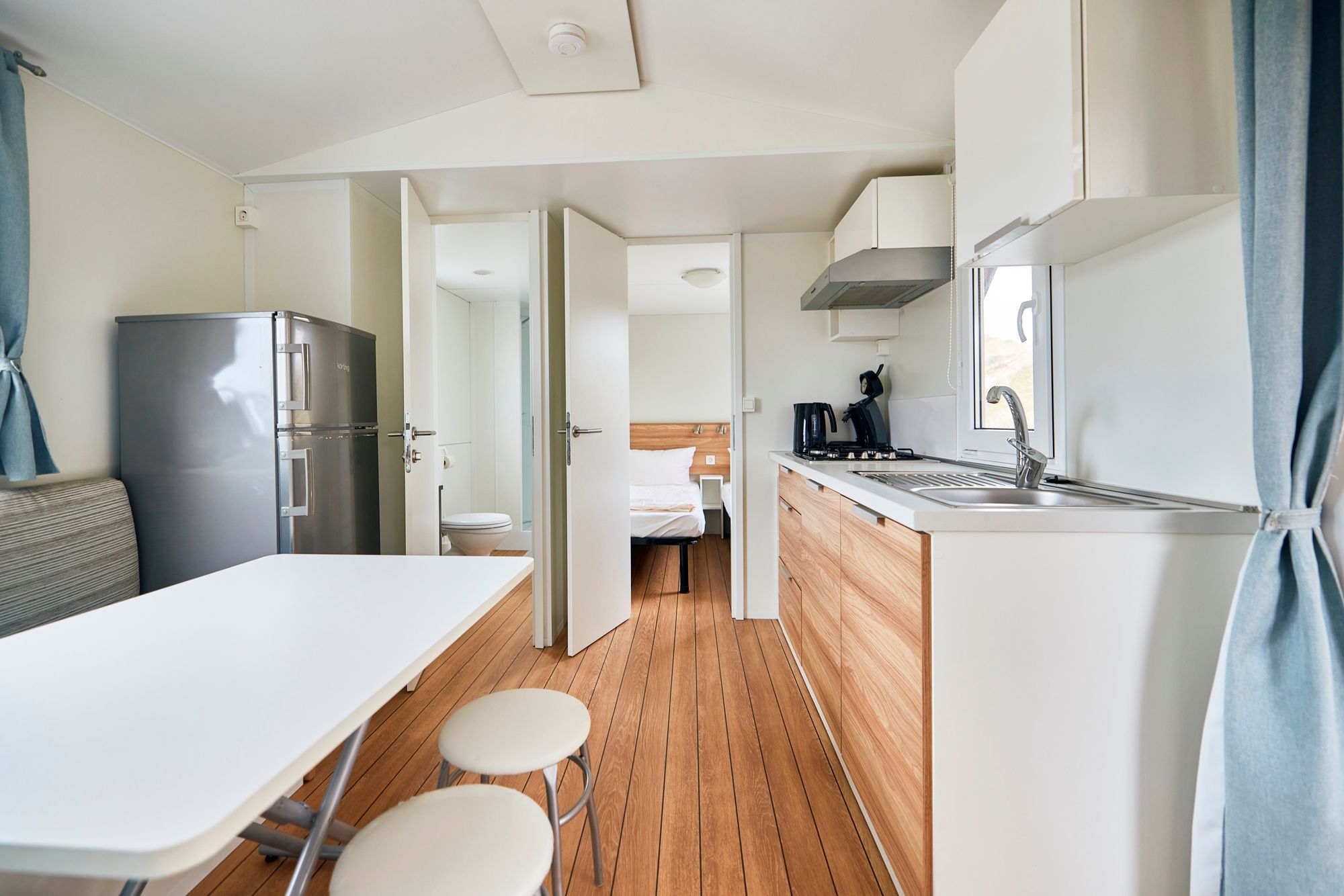 Essbereich und Küche mit Blick auf Badezimmer und ein Schlafzimmer im Familien-Mobilheim auf dem Campingplatz Westerland