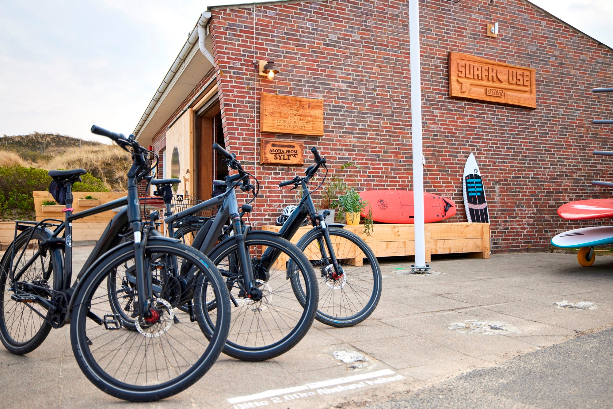 Drei E-Bikes stehen vor dem Surfhouse Sylt