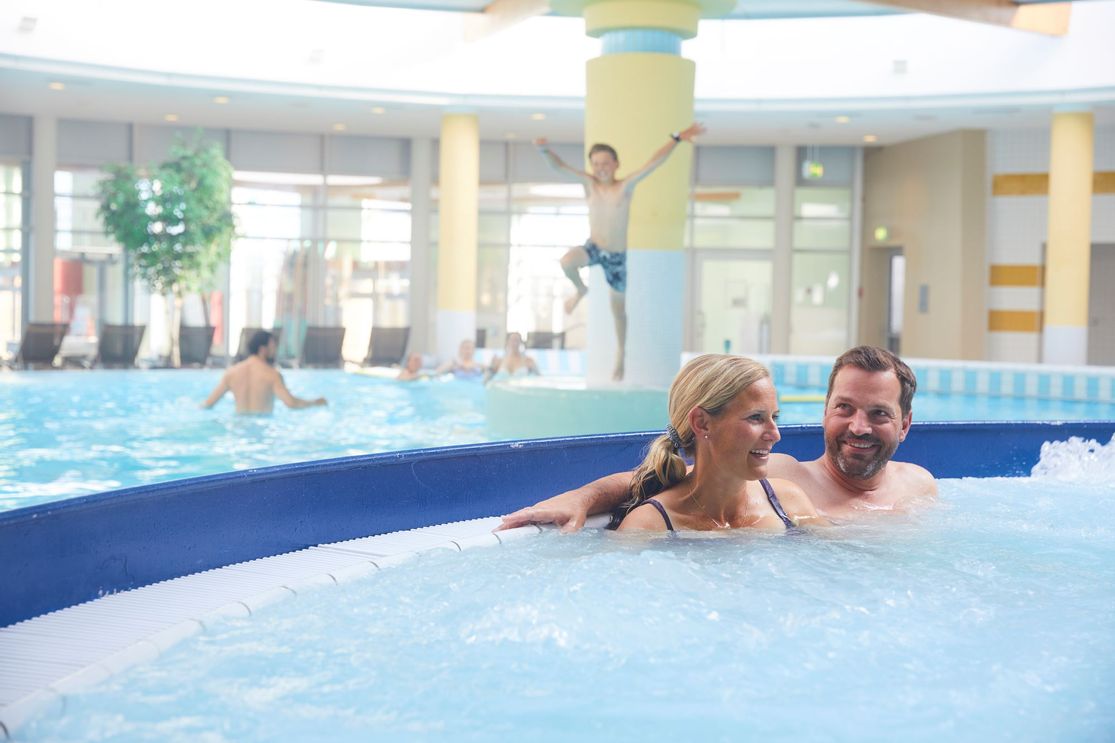 Mann und Frau sitzen im Massagebecken der Sylter Welle, in Hintergrund spielende und schwimmende Kinder im Sprudelbecken