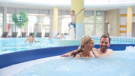 Mann und Frau sitzen im Massagebecken der Sylter Welle, in Hintergrund spielende und schwimmende Kinder im Sprudelbecken