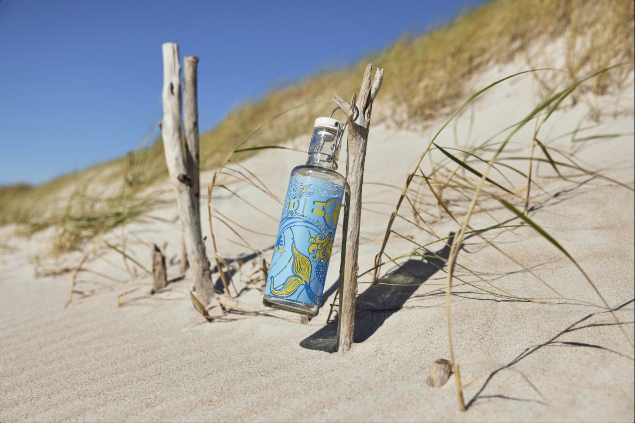 Die Wasserflasche von Sonni Hönscheid gestaltet, SyltBuddel genannt, hängt an einem Holz am Strand von Westerland