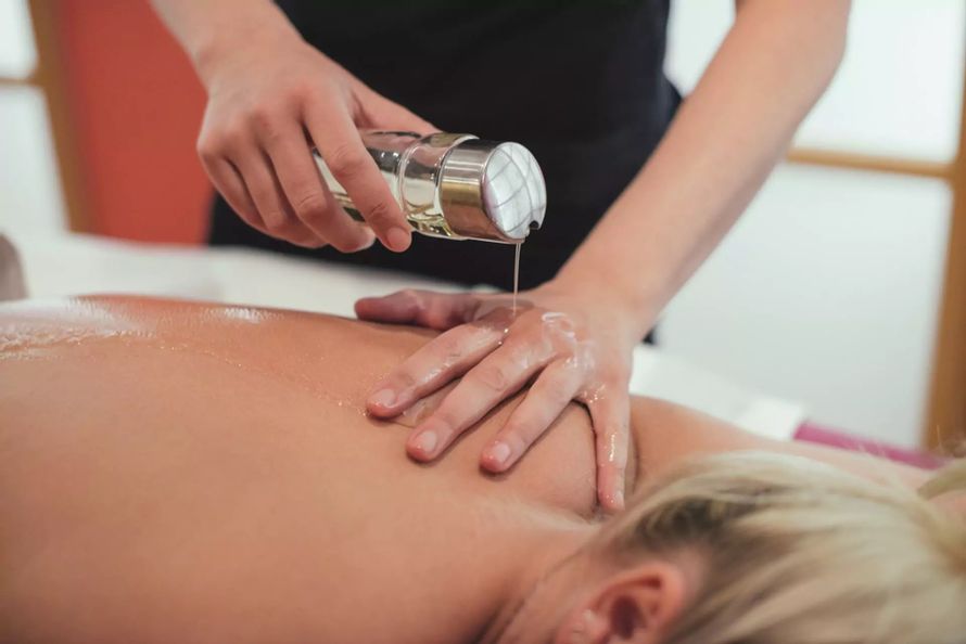 Frau gießt einer anderen Frau bei einer Wellnessmassage Öl auf den Rücken