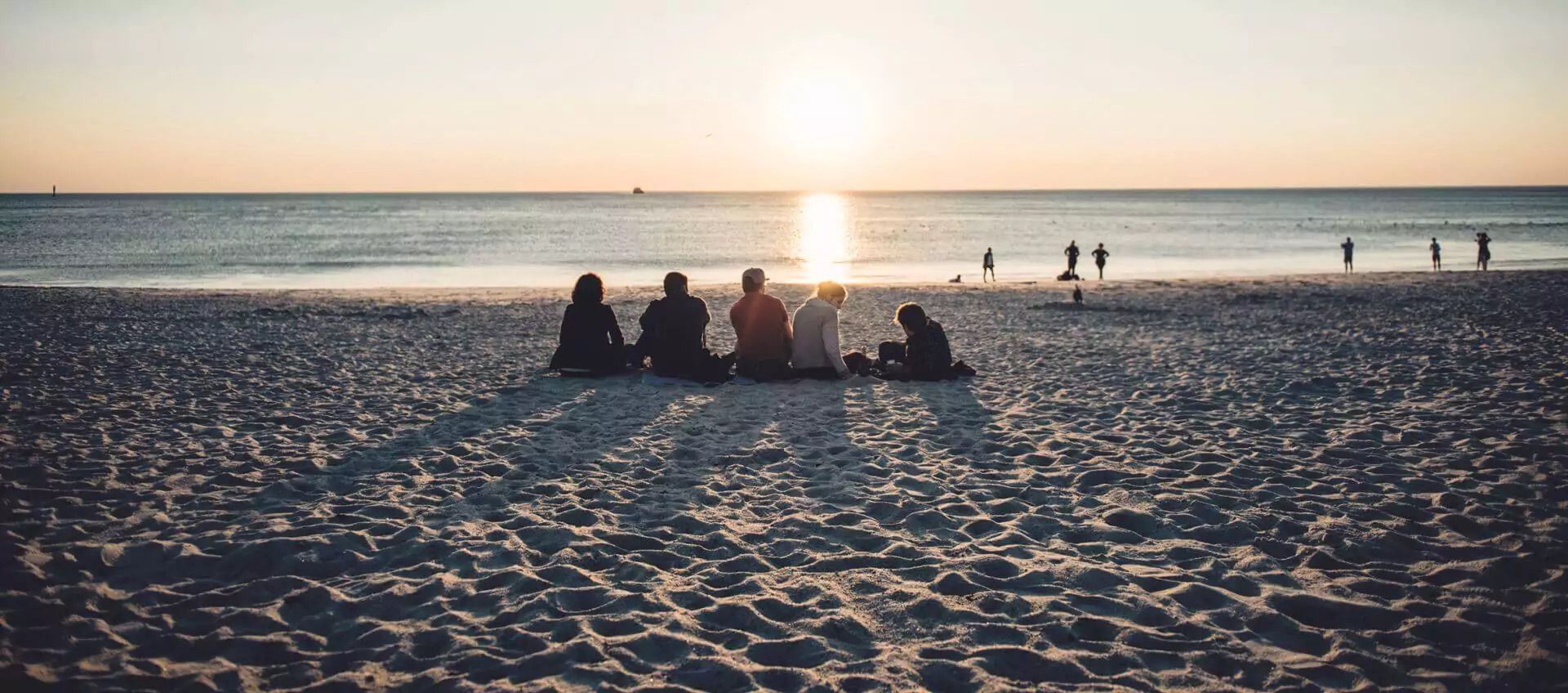 Fünf Personen schauen am Strand den Sonnenuntergang
