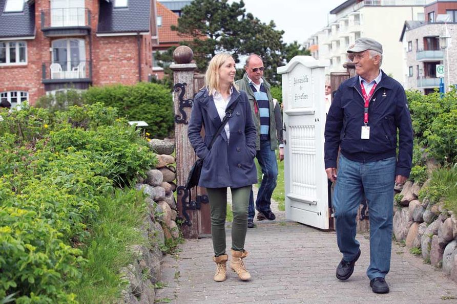 Eine Frau unterhält sich mit dem Gästeführer gehend vor dem Friedhof der Heimatlosen, im Hintergrund läuft ein Mann durch das Tor