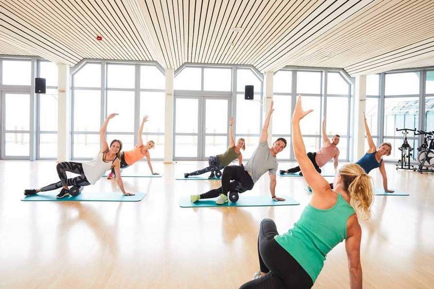 Gruppe aus 6 Personen macht die Übungen der Sportleiterin im Sportcenter nach