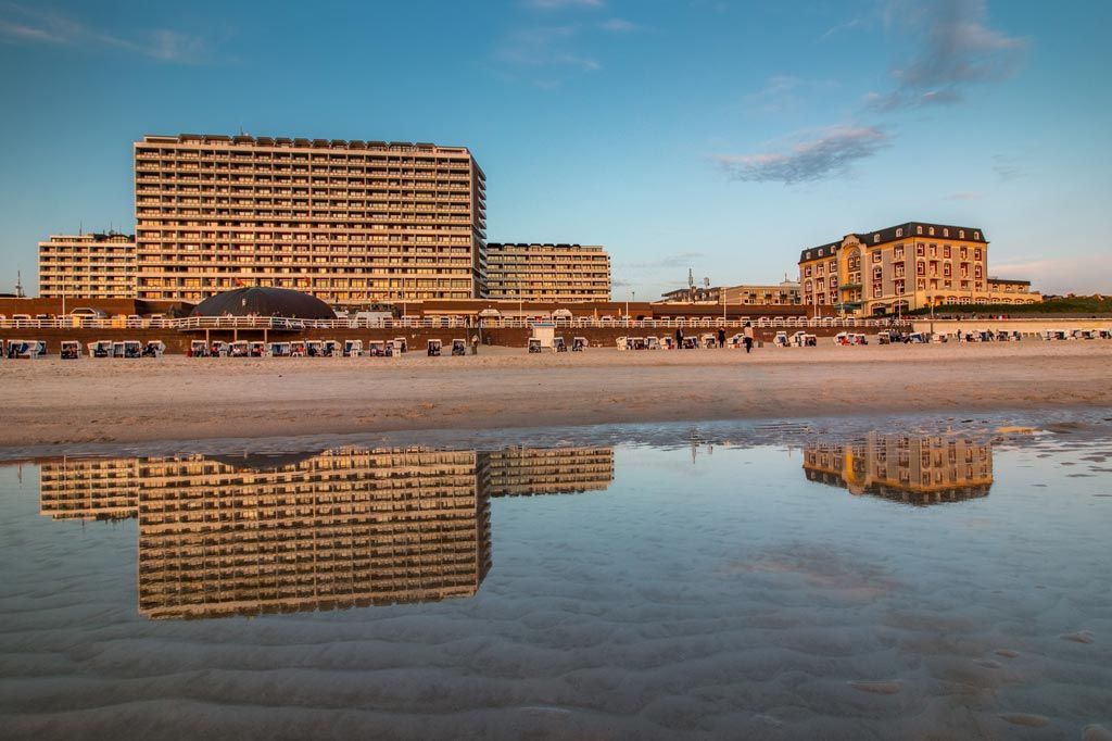 Blick vom Strand von Westerland auf das Kurzentrum, im Vordergrund spiegelt sich dieses und dazwischen stehen Strandkörben im Sand.