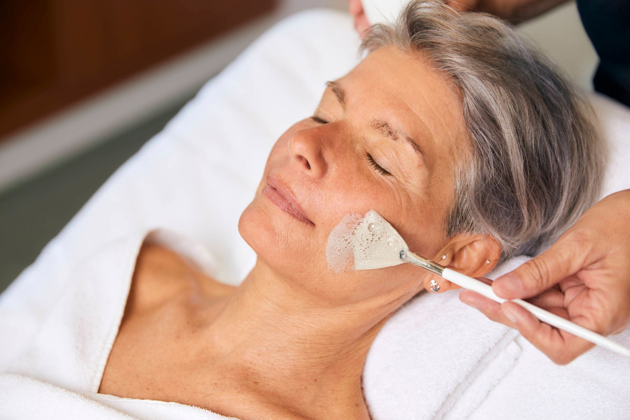 Frau bekommt mittels Pinsel eine Creme auf das Gesicht aufgetragen bei einer Gesichtsbehandlung im Syltness Center