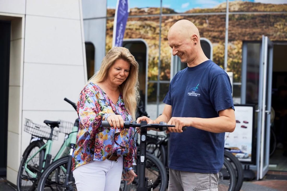 Männlicher Mitarbeiter zeigt weiblicher Kundin das gemietete E-Bike vor dem E-Mobility Center in Westerland auf Sylt