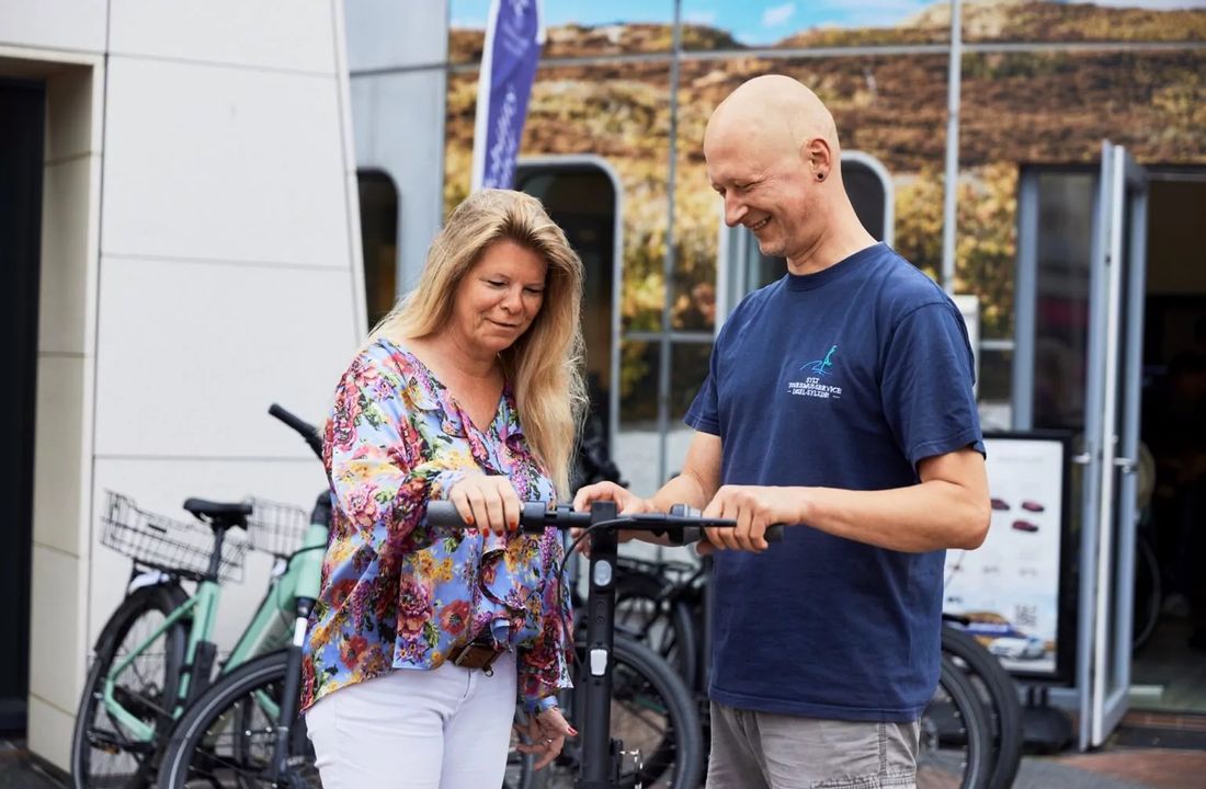 Männlicher Mitarbeiter zeigt weiblicher Kundin das gemietete E-Bike vor dem E-Mobility Center in Westerland auf Sylt