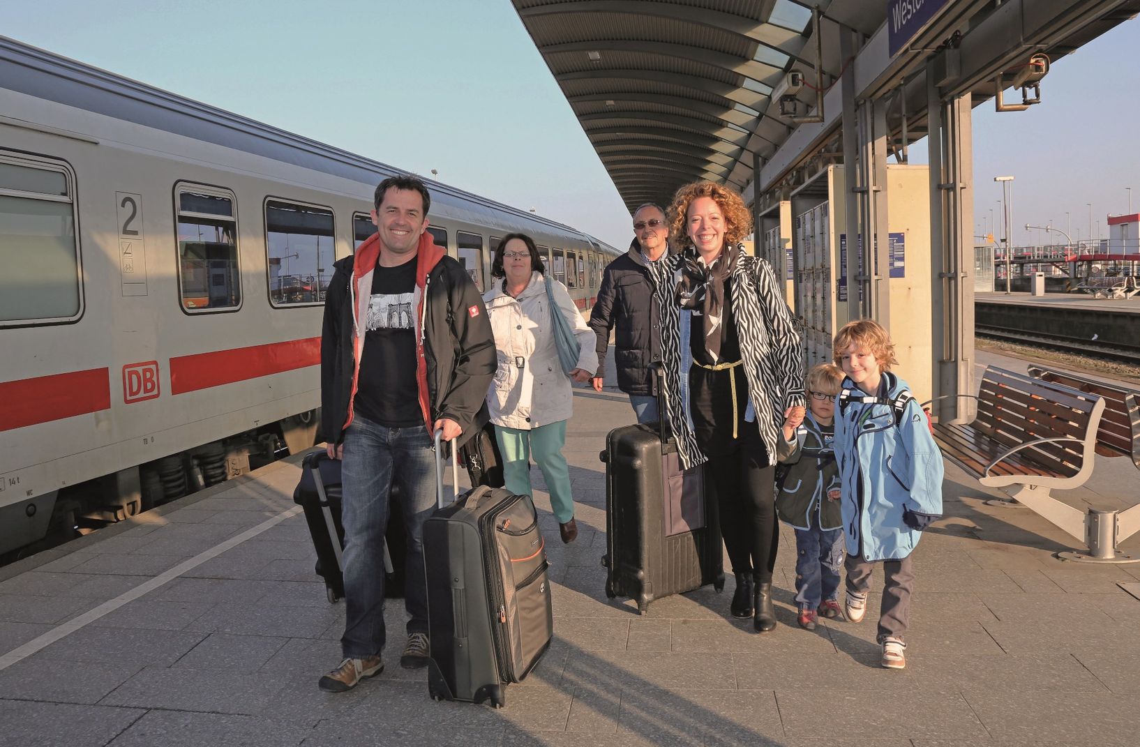 Eine Familie (Vater, Mutter, zwei Söhne, Großmutter und Großvater) sind soeben mit den Zug am Bahnhof Westerland angereist und laufen freudestrahlend mit ihren Koffern der Kamera entgehen