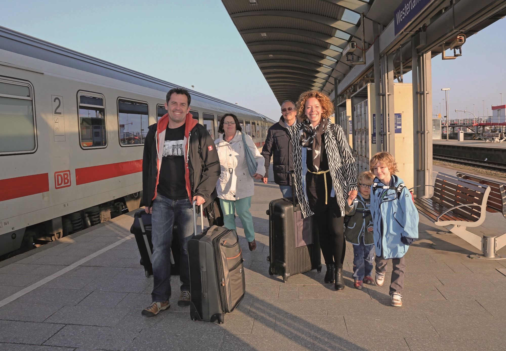 Eine Familie (Vater, Mutter, zwei Söhne, Großmutter und Großvater) sind soeben mit den Zug am Bahnhof Westerland angereist und laufen freudestrahlend mit ihren Koffern der Kamera entgehen