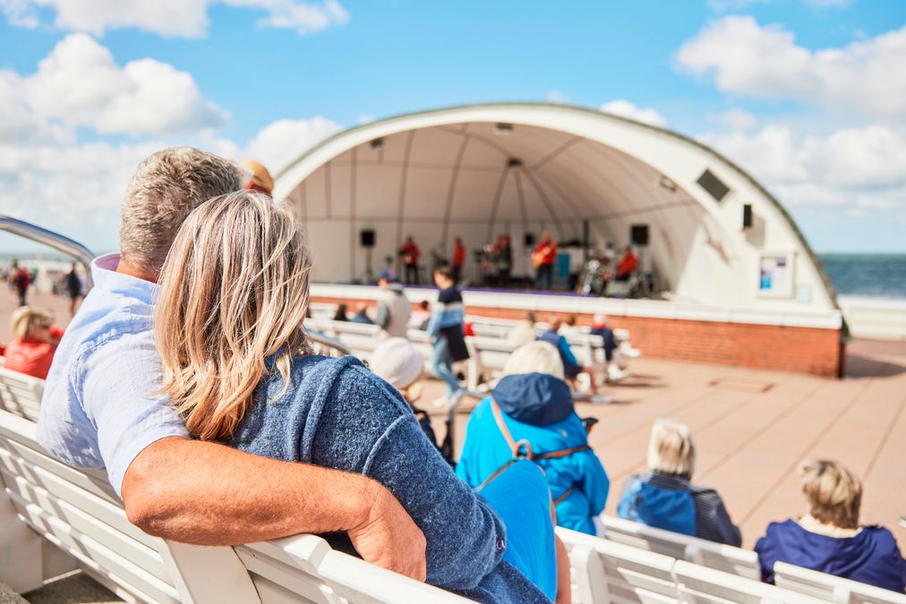 Mann und Frau sitzen auf den Bänken vor der Musikmuschel und lauschen der Musik am Meer