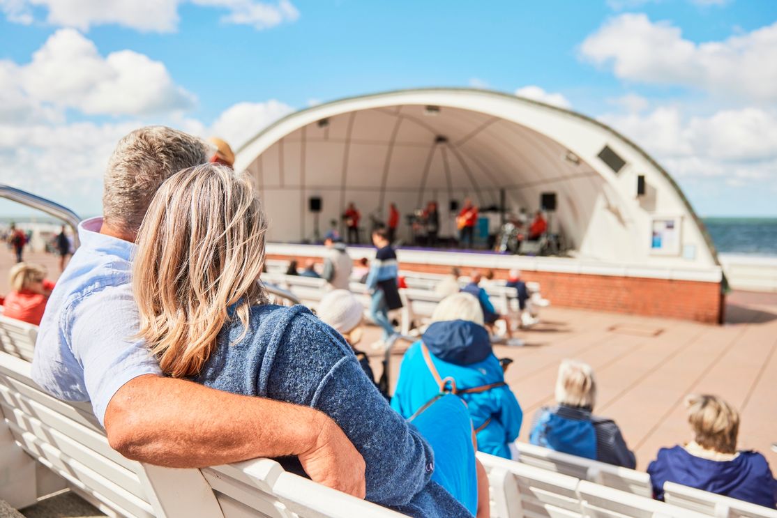 Mann und Frau sitzen auf den Bänken vor der Musikmuschel und lauschen der Musik am Meer