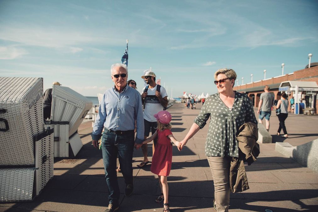 Älteres Paar, Mann und Frau, spazieren freudig strahlend mit jungem Mädchen über die Westerländer Promenade