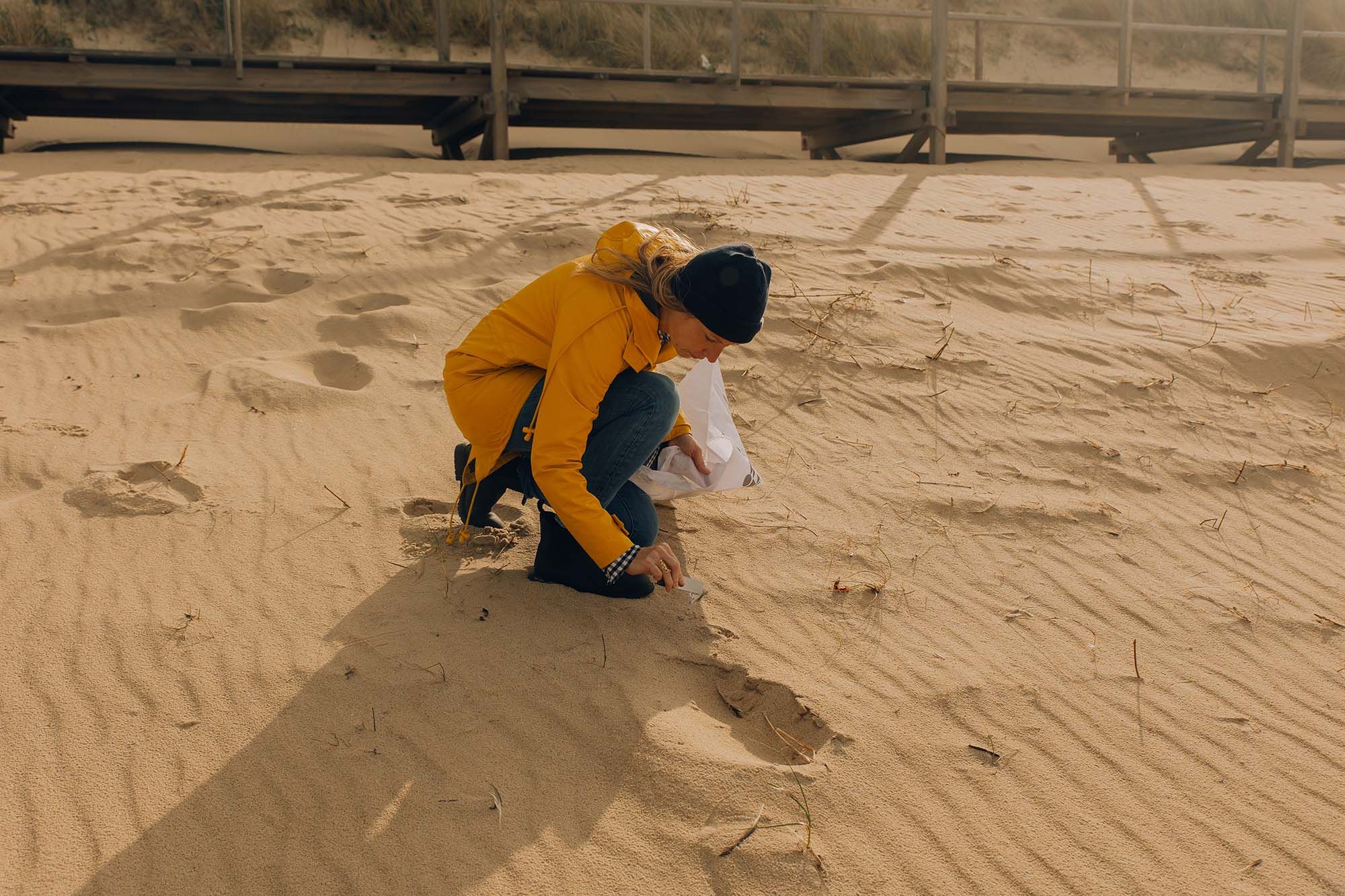 Frau sammelt in gelber Regenjacke Müll am Strand bei den Clean Up Days Sylt