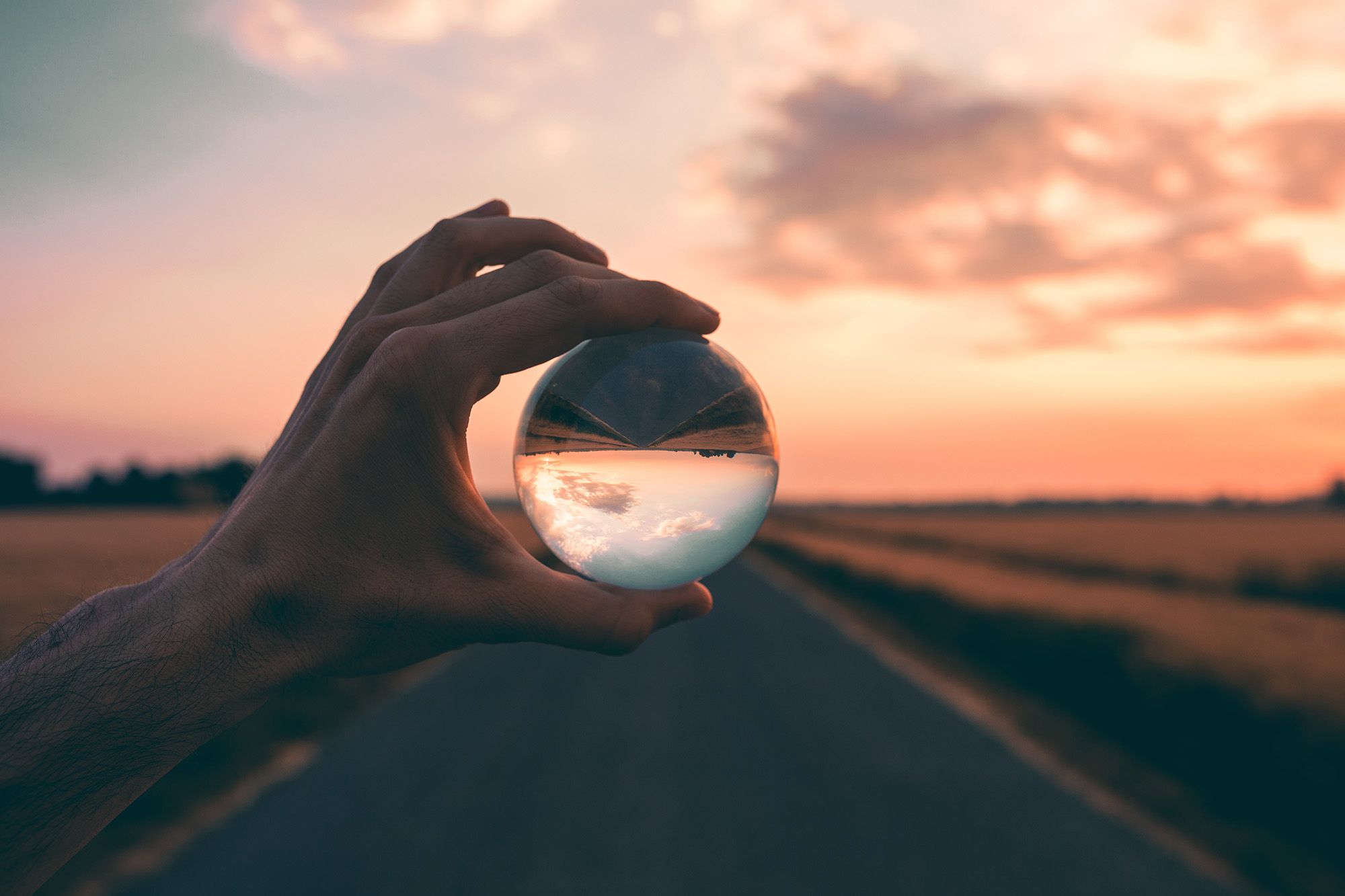 Person hält Glaskugel gegen Sonnenuntergang