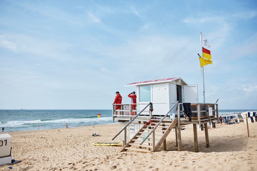 Zwei Rettungsschwimmer stehen auf einem Rettungsschwimmerstand am Strand von Westerland auf Sylt und halten Ausschau auf Badende in der Nordsee