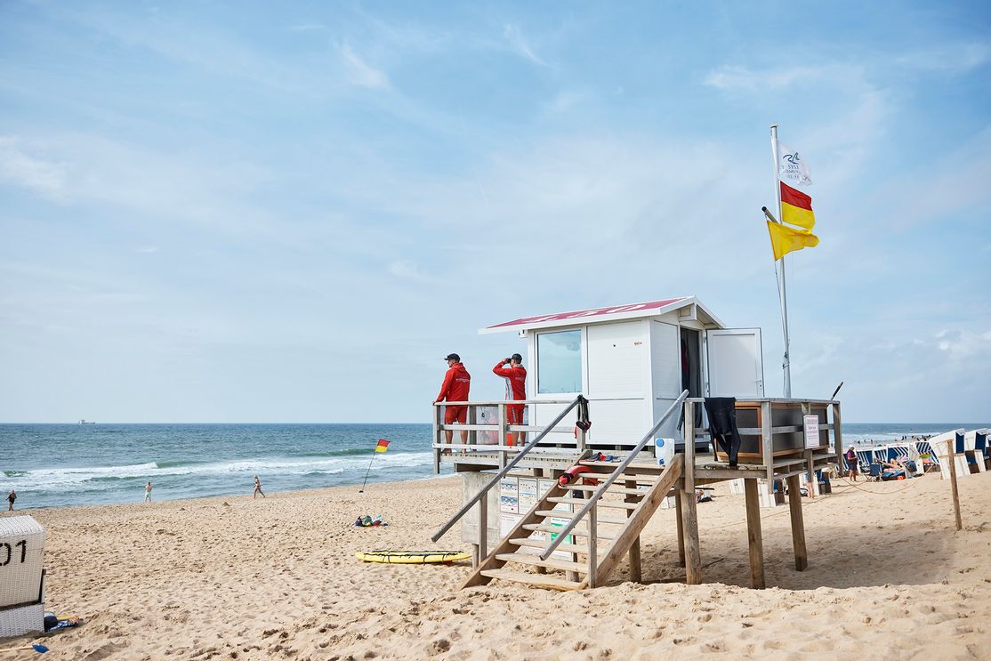 Zwei Rettungsschwimmer stehen auf einem Rettungsschwimmerstand am Strand von Westerland auf Sylt und halten Ausschau auf Badende in der Nordsee